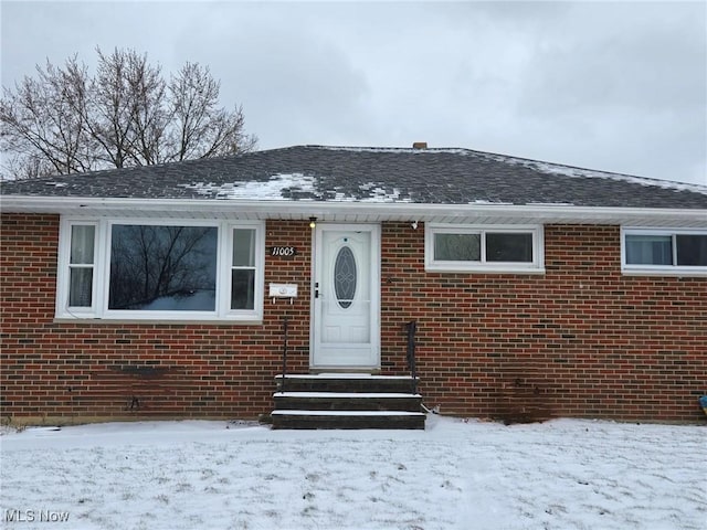 snow covered property entrance with brick siding and roof with shingles