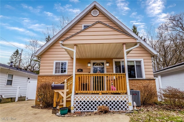 view of front of home with covered porch, brick siding, and cooling unit