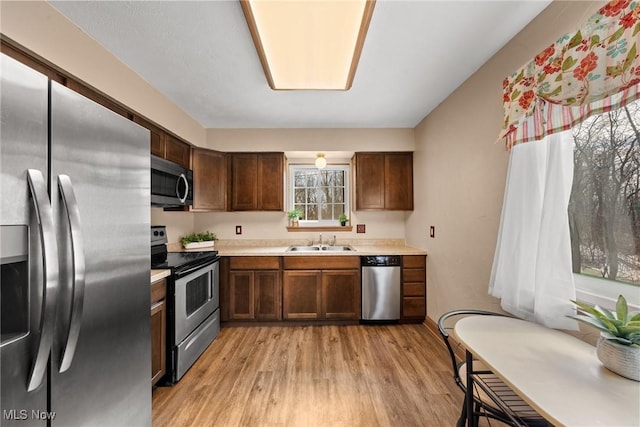 kitchen with appliances with stainless steel finishes, light countertops, a sink, and light wood finished floors