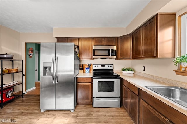 kitchen with stainless steel appliances, light countertops, a sink, and light wood-style flooring