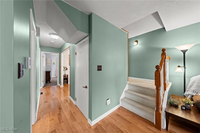 hall with light wood finished floors, stairs, and baseboards