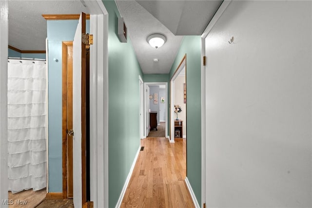 hall featuring light wood finished floors, baseboards, and a textured ceiling