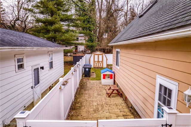 exterior space with a shingled roof, fence private yard, a storage unit, an outdoor structure, and a patio area