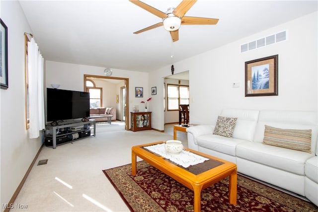 living room featuring a ceiling fan, visible vents, light carpet, and baseboards