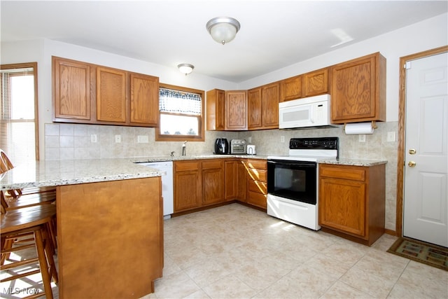 kitchen with tasteful backsplash, a peninsula, white appliances, and brown cabinets