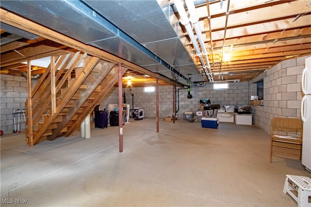 unfinished basement with stairway and freestanding refrigerator