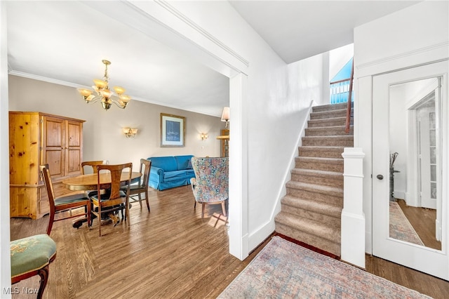 stairs featuring crown molding, an inviting chandelier, wood finished floors, and baseboards