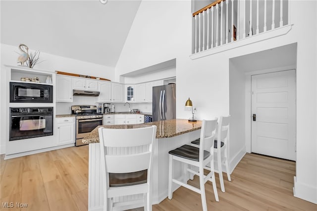 kitchen with dark stone counters, black appliances, white cabinets, and under cabinet range hood