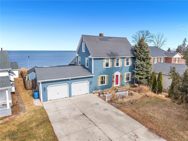 colonial inspired home with roof with shingles, a chimney, a water view, an attached garage, and driveway