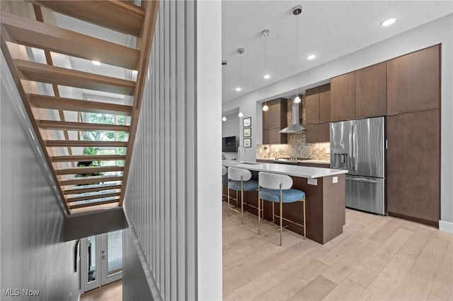 kitchen featuring a breakfast bar, wall chimney exhaust hood, tasteful backsplash, modern cabinets, and stainless steel fridge