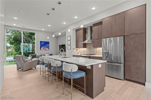 kitchen with stainless steel appliances, open floor plan, wall chimney range hood, modern cabinets, and a kitchen bar