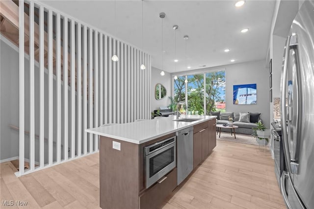 kitchen with a sink, open floor plan, appliances with stainless steel finishes, light wood-type flooring, and modern cabinets