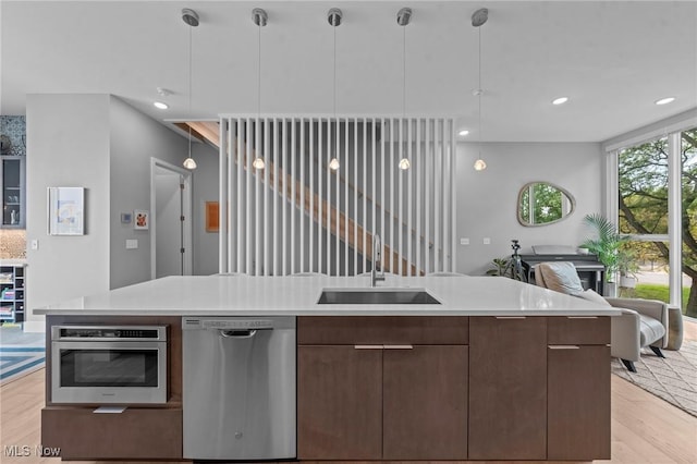 kitchen featuring modern cabinets, stainless steel appliances, light countertops, light wood-type flooring, and a sink