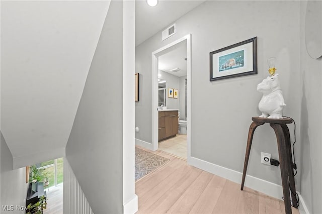 hallway with visible vents, light wood-style flooring, and baseboards