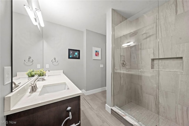 bathroom with double vanity, a stall shower, baseboards, and a sink