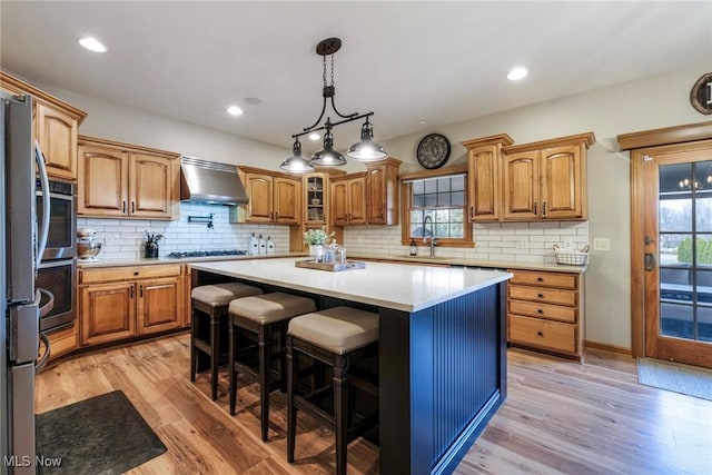 kitchen with wall chimney exhaust hood, a kitchen island, a sink, and light wood-style floors