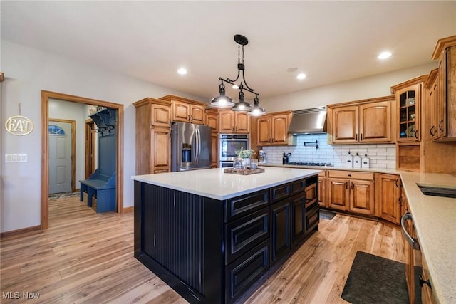 kitchen with appliances with stainless steel finishes, backsplash, light wood finished floors, and ventilation hood