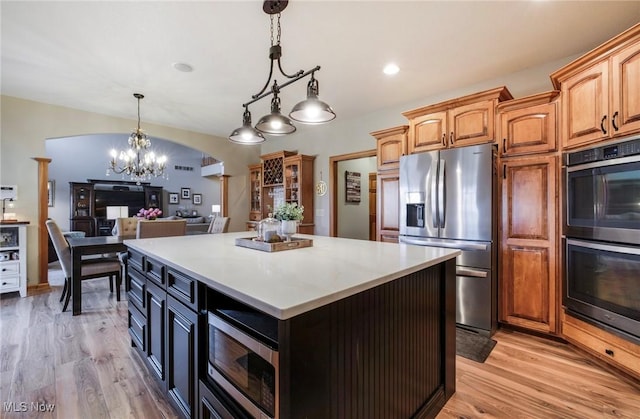 kitchen with arched walkways, light wood finished floors, stainless steel appliances, hanging light fixtures, and a kitchen island