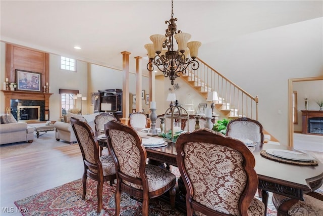 dining area featuring a towering ceiling, wood finished floors, an inviting chandelier, a fireplace, and recessed lighting