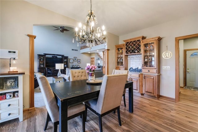 dining area featuring arched walkways, light wood-style floors, a ceiling fan, vaulted ceiling, and baseboards