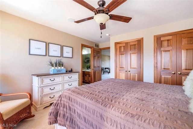 bedroom featuring visible vents, light colored carpet, ceiling fan, ensuite bathroom, and multiple closets