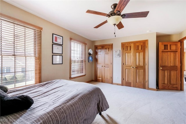 carpeted bedroom featuring multiple closets, ceiling fan, and baseboards