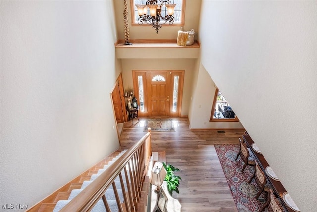 entryway with wood finished floors, a towering ceiling, and an inviting chandelier