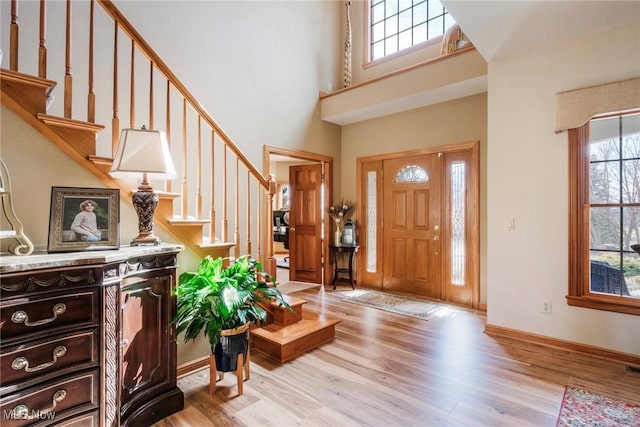 foyer with light wood finished floors, stairway, plenty of natural light, and a towering ceiling