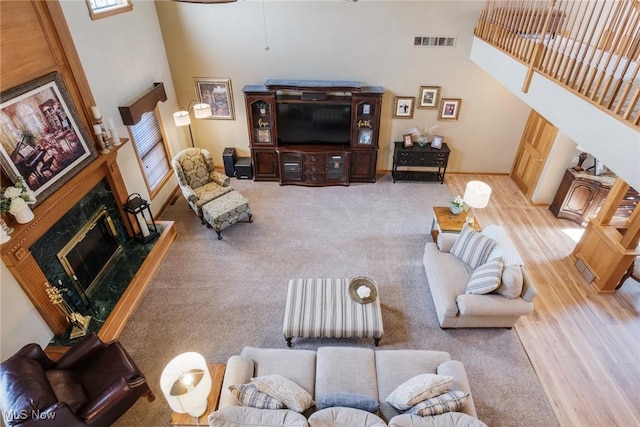 living area featuring carpet flooring, visible vents, a high ceiling, and a premium fireplace