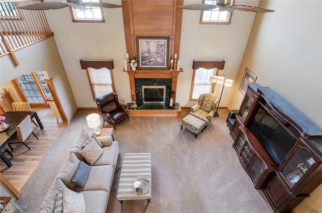 living room with a healthy amount of sunlight, a towering ceiling, a high end fireplace, and a ceiling fan