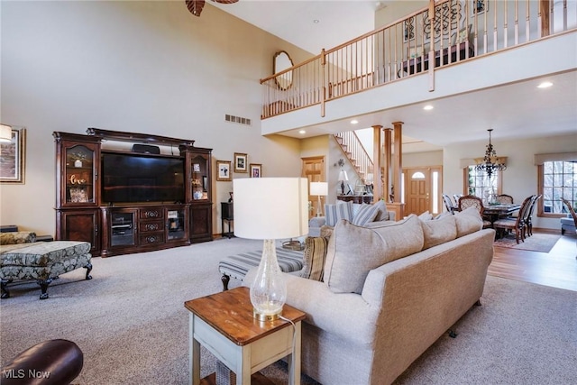 carpeted living area featuring decorative columns, visible vents, stairway, a high ceiling, and recessed lighting