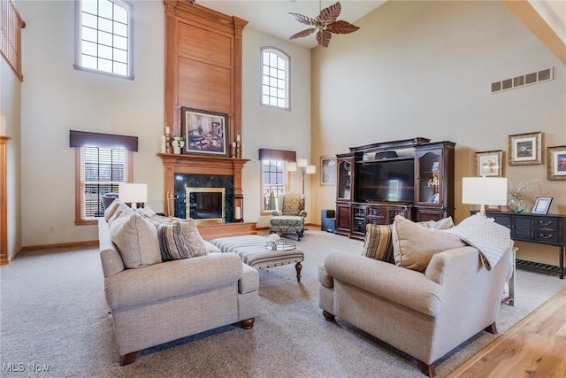 living area featuring a fireplace, visible vents, a towering ceiling, light carpet, and baseboards