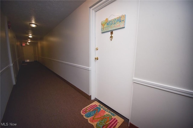 hallway featuring dark colored carpet, a textured ceiling, and baseboards