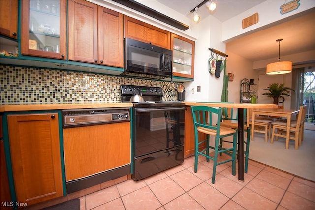 kitchen featuring pendant lighting, light countertops, backsplash, glass insert cabinets, and black appliances