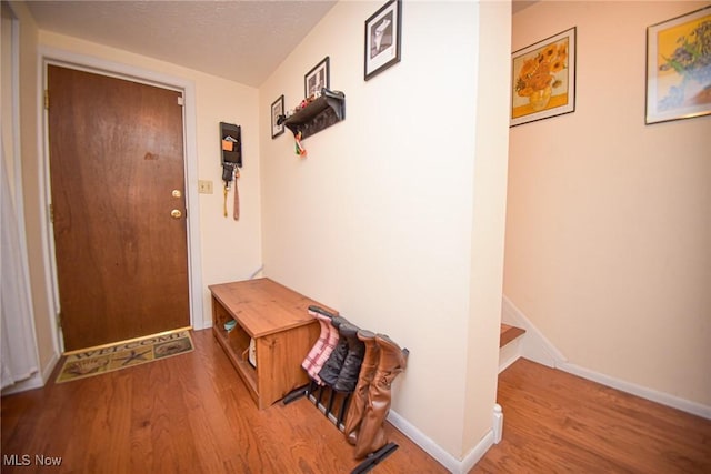 hall with stairway, a textured ceiling, baseboards, and wood finished floors