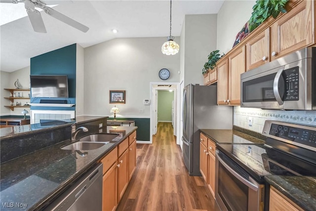 kitchen with lofted ceiling, appliances with stainless steel finishes, a sink, wood finished floors, and dark stone counters