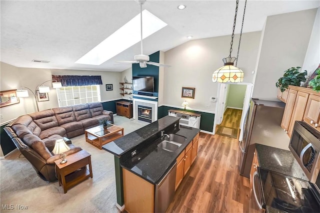 living area featuring a fireplace, wood finished floors, visible vents, a ceiling fan, and lofted ceiling with skylight