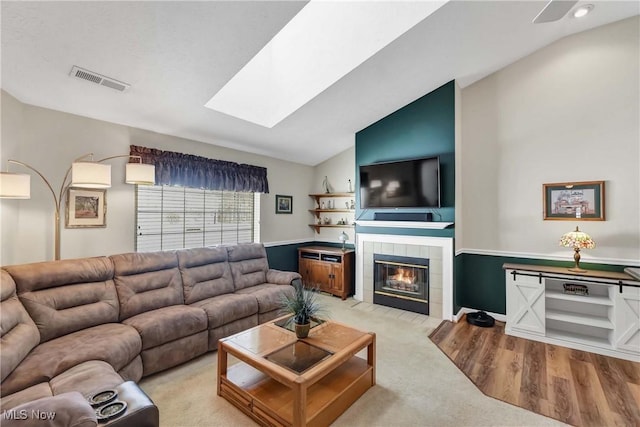 living room featuring vaulted ceiling with skylight, a fireplace, visible vents, and wood finished floors