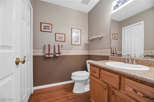 bathroom with toilet, wood finished floors, vanity, visible vents, and baseboards