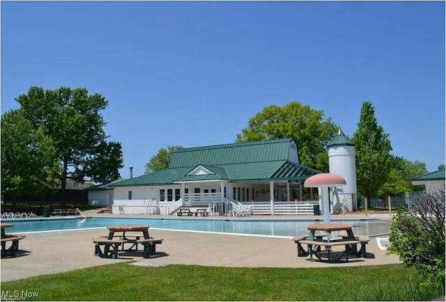 rear view of property with a patio area, a community pool, metal roof, and a standing seam roof