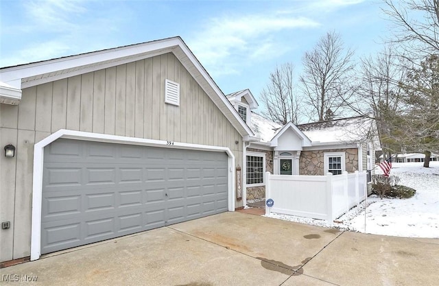 exterior space with stone siding, an attached garage, concrete driveway, and fence