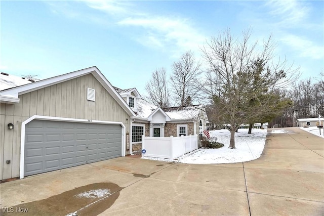 view of home's exterior featuring a garage, concrete driveway, stone siding, and fence