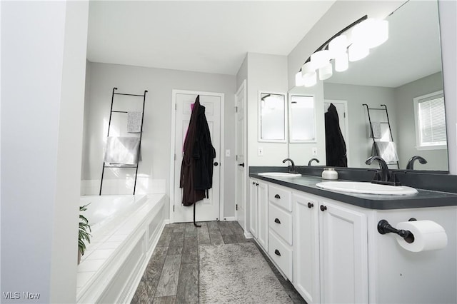 full bathroom featuring double vanity, a sink, a bathing tub, and wood finished floors