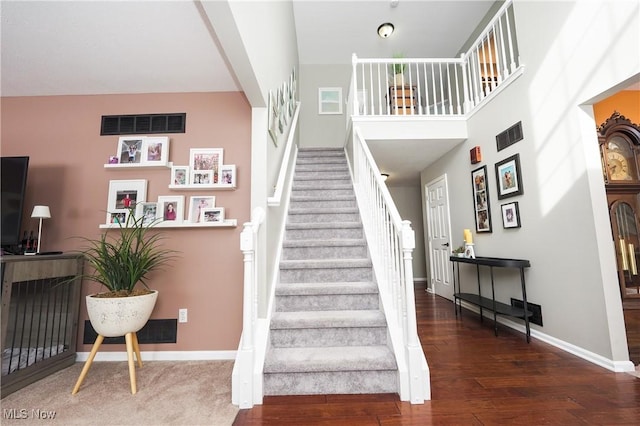 staircase with a towering ceiling, wood finished floors, visible vents, and baseboards