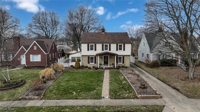 view of front facade featuring a front yard, stone siding, fence, and a chimney