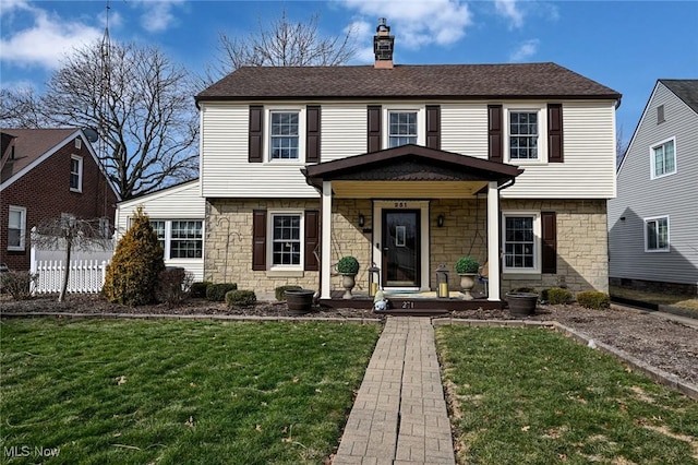 colonial-style house featuring stone siding, a chimney, roof with shingles, fence, and a front yard