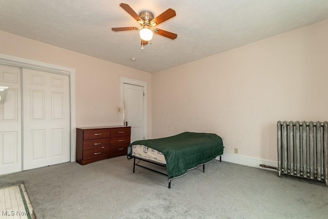 bedroom featuring light carpet, baseboards, a ceiling fan, radiator, and a closet