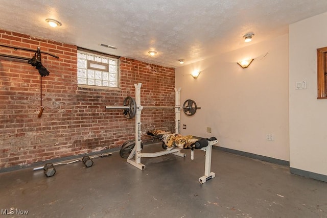 exercise area featuring brick wall, baseboards, visible vents, and a textured ceiling