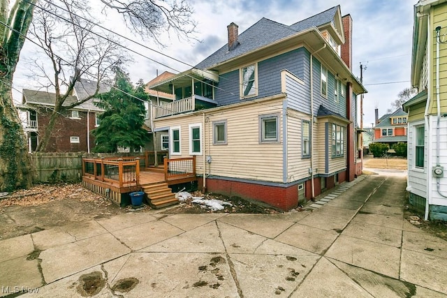 rear view of house featuring a balcony, a chimney, fence, and a deck