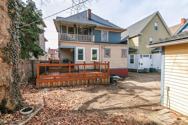 rear view of property with a balcony, a chimney, and fence